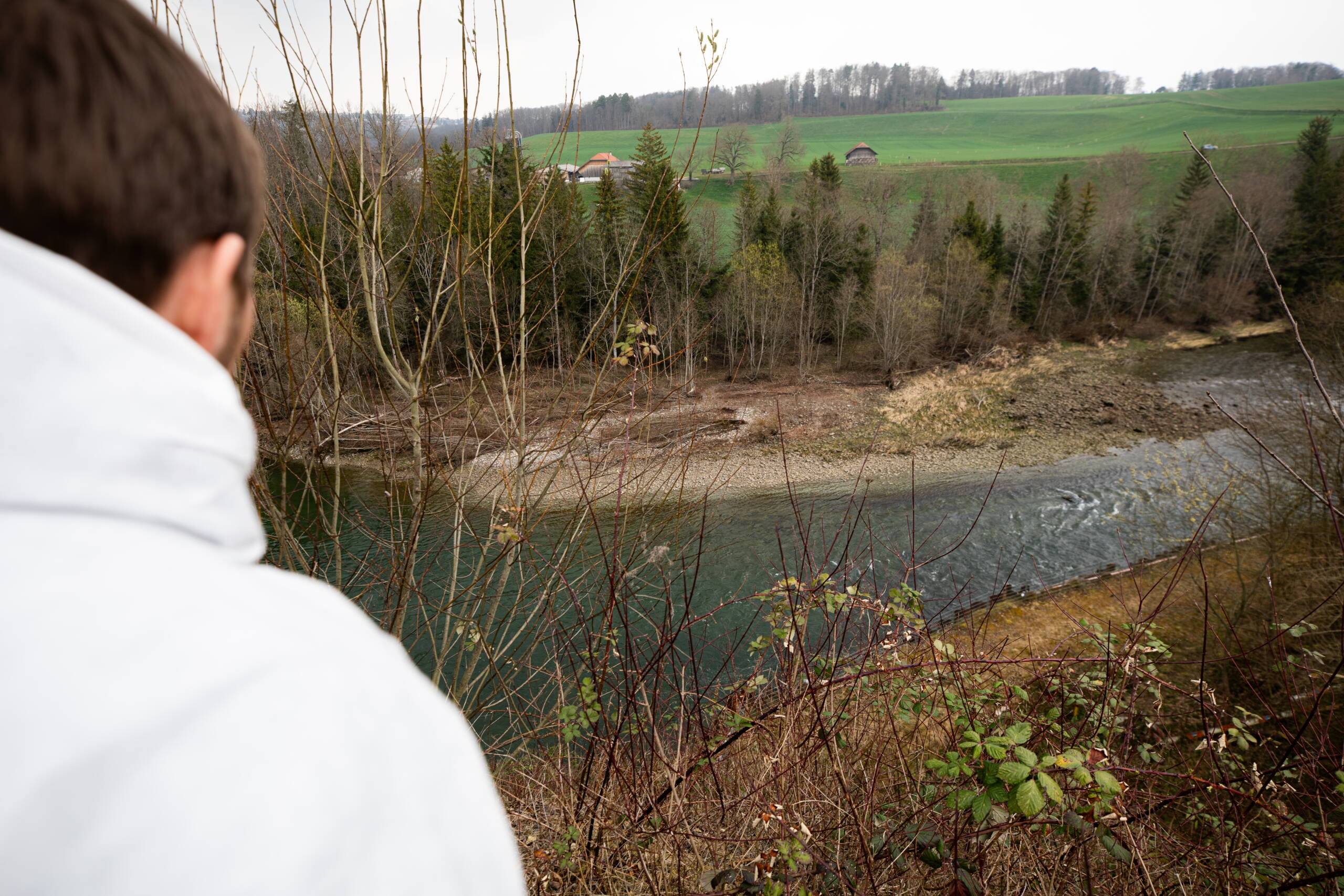 La vue depuis le sommet de la décharge montre qu'une pente raide recouverte de déchets envahis par la végétation mène directement aux rives de la Sarine. 