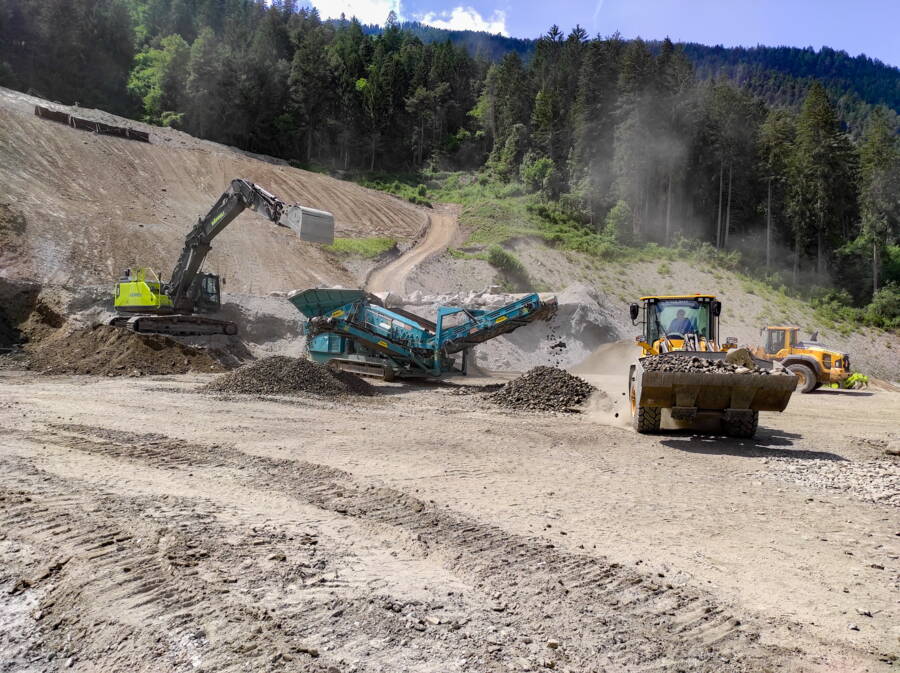 Aufbereitung von Material aus dem Hangabtrag für die projektgemässen Verwertungen. In der Mitte die Siebanlage, die mit dem 40to Bagger beschickt wird.